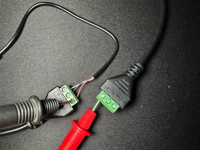 Deux sondes de multimètre en mode continuité testent la correspondance des bornes L d'un câblage électronique.